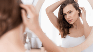 鏡を見ながら髪をチェックする女性。白髪や薄毛の悩みを抱え、真剣な表情をしています。Manoukian麻布台の「白髪薄毛改善Manouシステム」で、髪の悩みを解決したいという気持ちを表現しています。