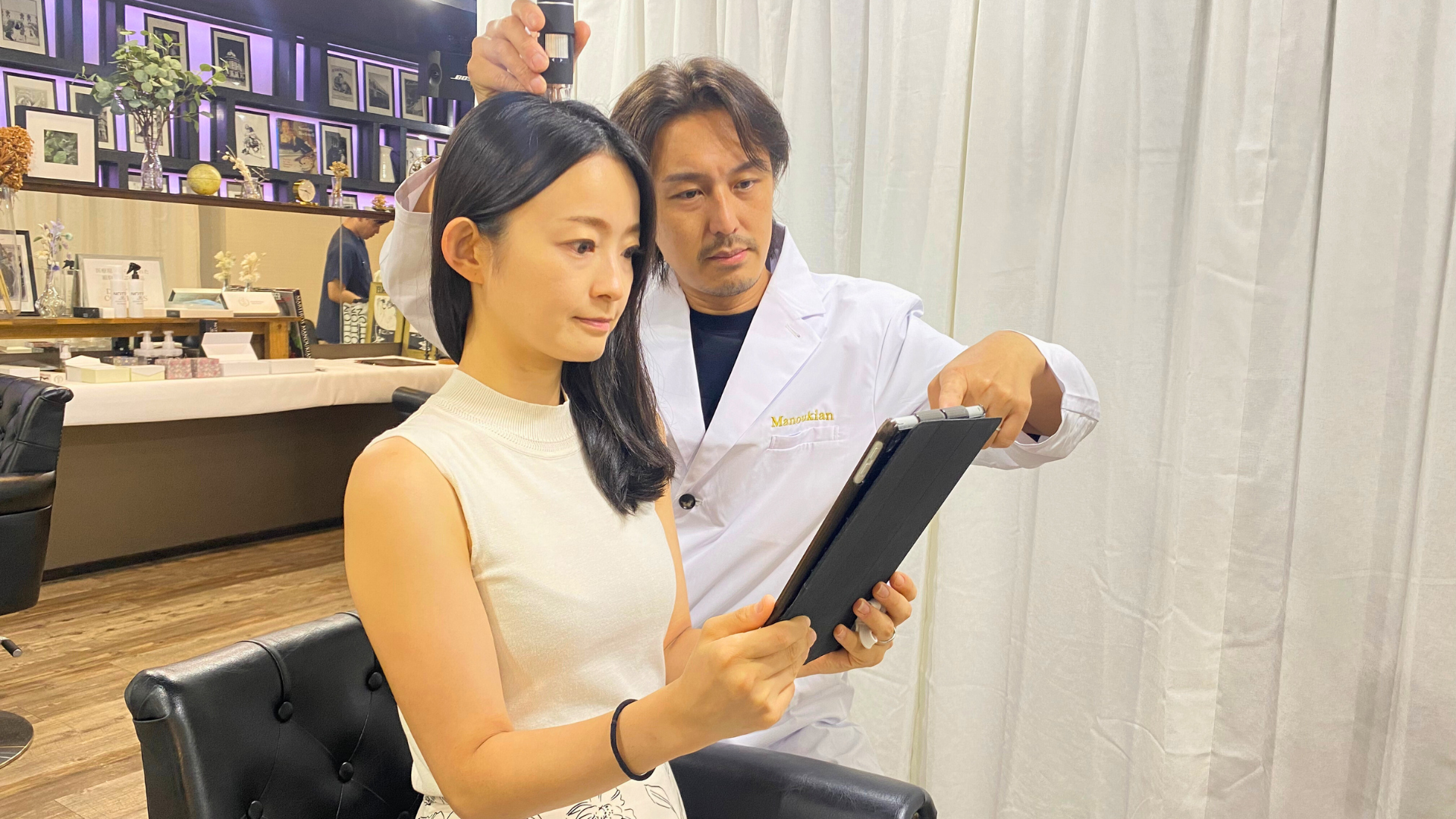 Manoukian麻布台の「再生育毛Manouシステム」について、専門家が女性のお客様にタブレットを使ってカウンセリングを行う様子