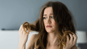髪の広がりやパサつきに悩み、自分の髪を見つめて困っている女性