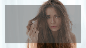 髪の乾燥、広がり、ダメージに深刻に悩んでいる様子の女性。髪の毛先を持ち、不安そうな表情を浮かべている。